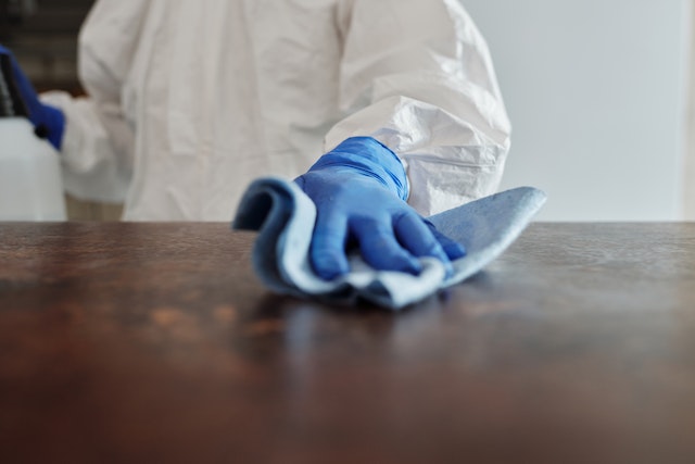 person in blue cleaning gloves and white coveralls cleaning a counter